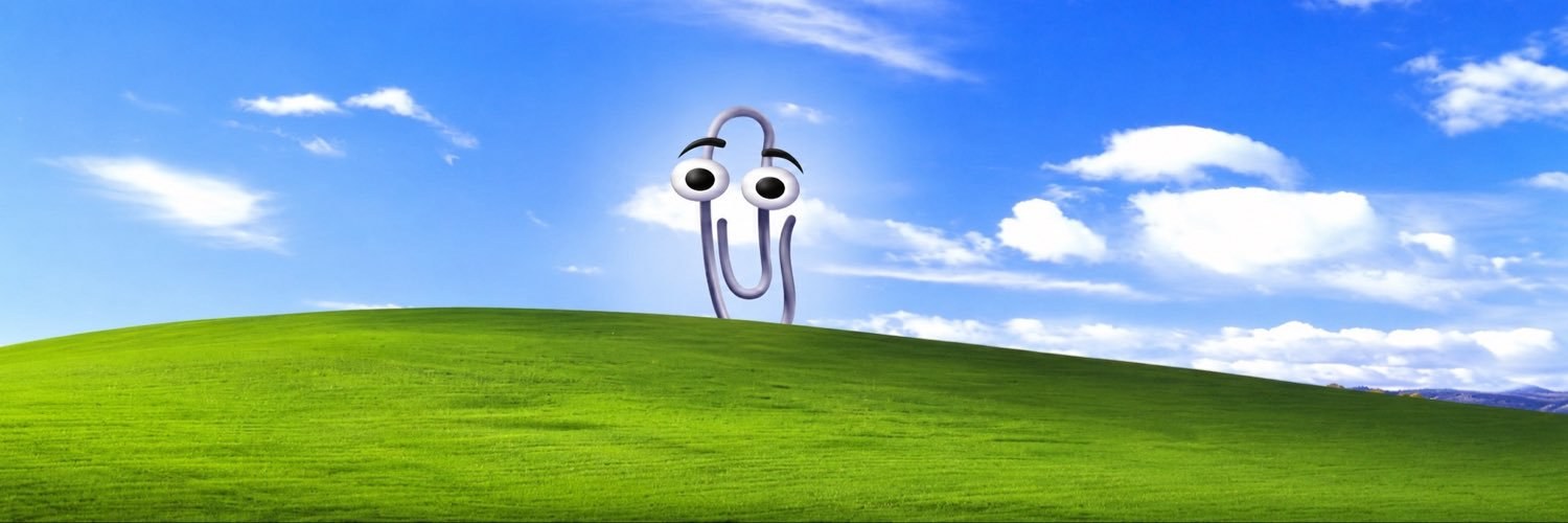 Clippy standing on a green hill under a wide blue sky